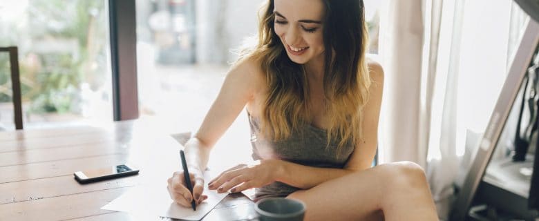 A young woman balances her checking account while enjoying a cup of coffee.