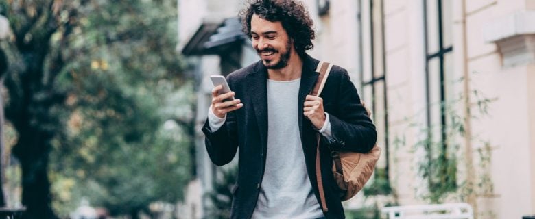 A young man with a beard smiles as he looks at his smart phone.