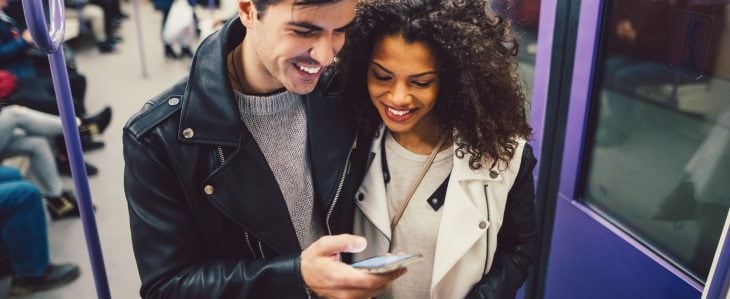 A man and a woman, riding the subway, look at something on a smart phone together.