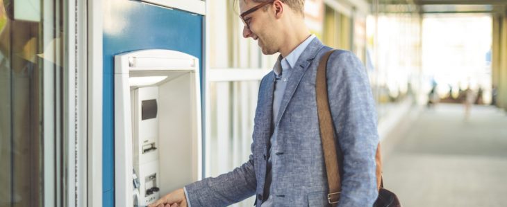 A man in business attire accesses cash from an ATM.
