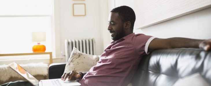 Person comfortably sits on a sofa and scrolls through their laptop.