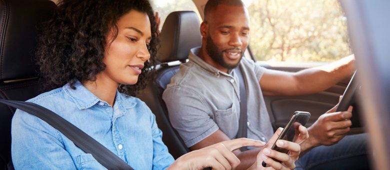 A couple sits in a car look at a mobile device.