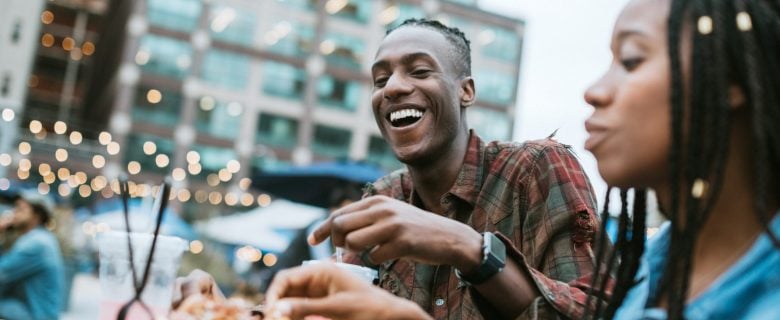 A man and a woman laughing together, as they enjoy a meal at an outside café.