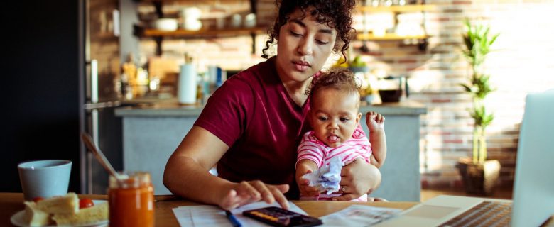 A woman, holding her baby, balances her budget using the 50-20-30 rule.