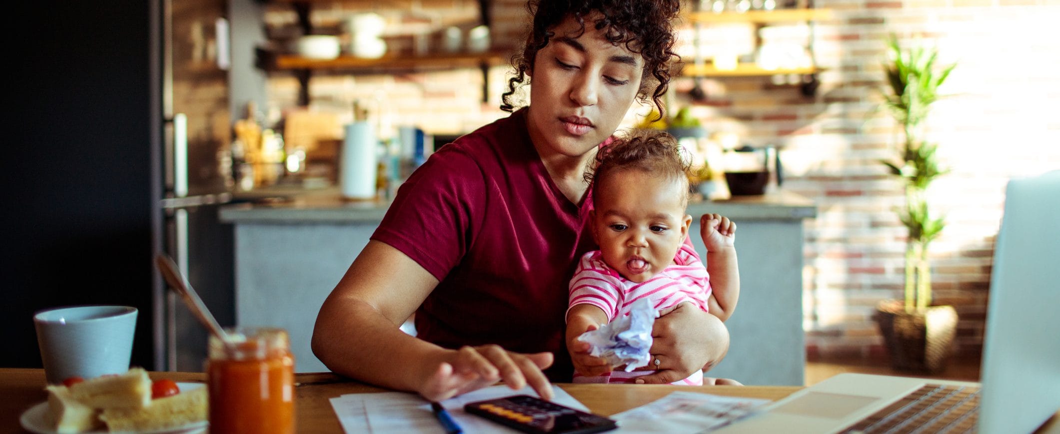 A woman, holding her baby, balances her budget using the 50-20-30 rule.
