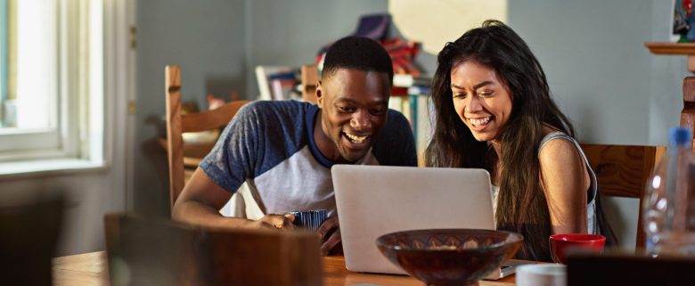 A man and a woman, sitting at their kitchen table, review their budget on a laptop computer.