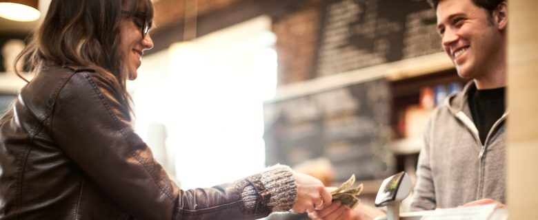 A woman hands money to a cashier at a shop.