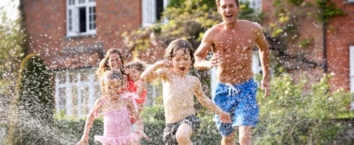A family runs through a sprinkler in a backyard.