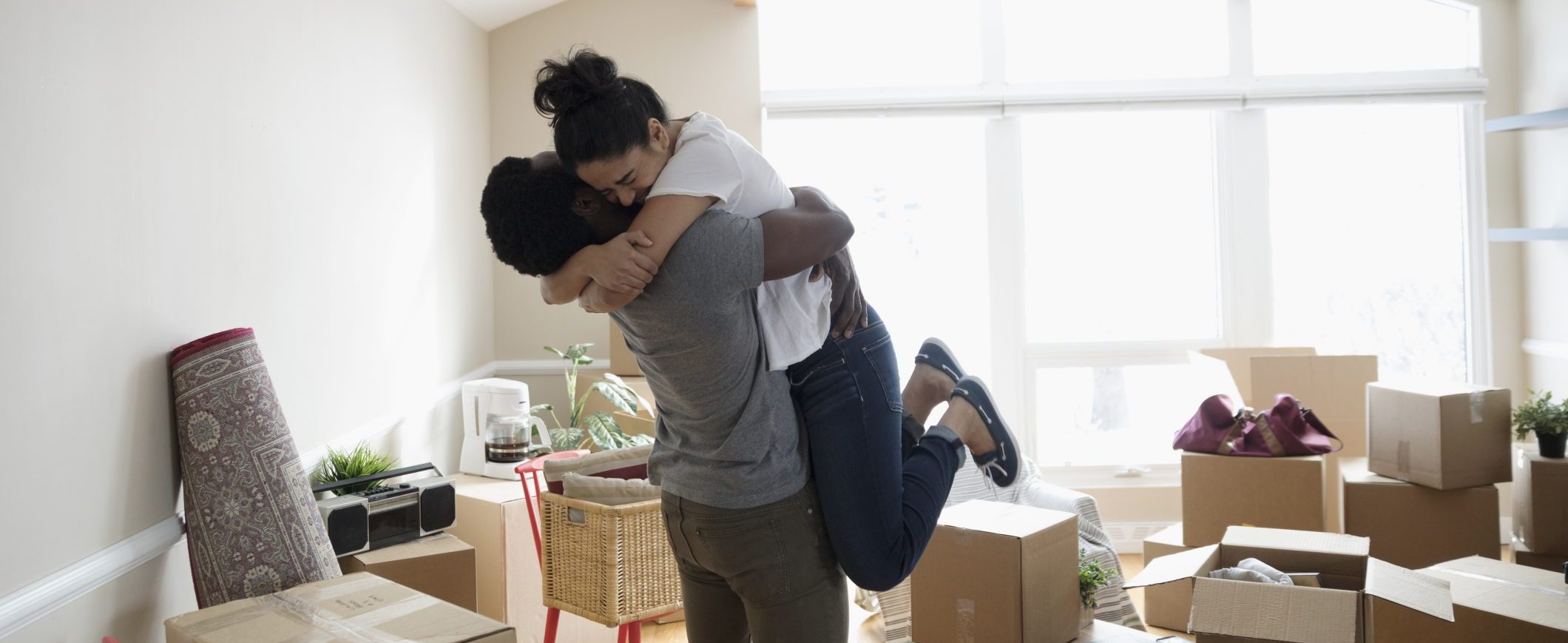 A man hugs a woman amongst a room full of boxes.