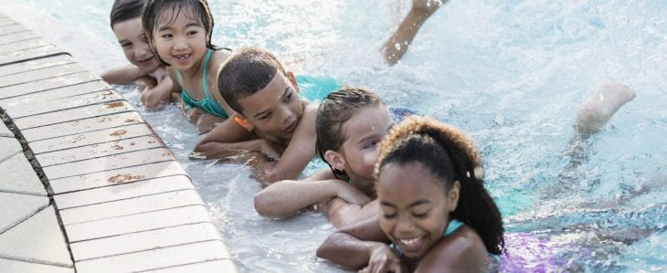 Five children hold the side of a pool and kick their legs in the water.