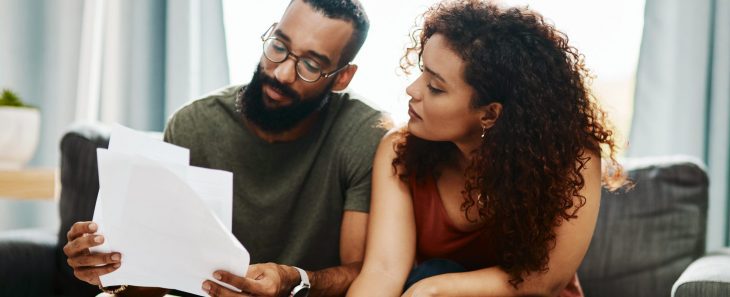 A man and a woman review documents together while sitting on their couch.