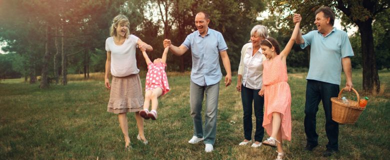 Parents, their two children, and the children's grandparents enjoy a walk in the park as they prepare for a picnic.