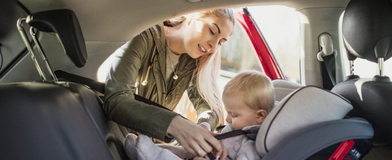 A woman buckles a baby into a car seat in the back seat of a vehicle. 