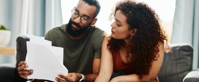 A couple sits on a couch and looks at some papers together. 