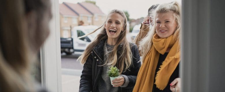 A group of smiling women at someone's door front.