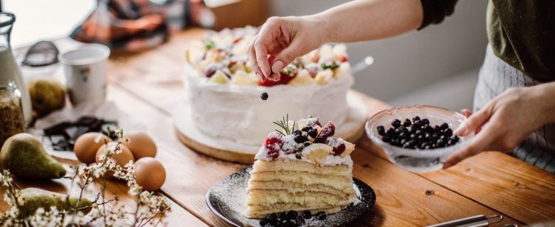 Closeup of a baker garnishing a slice of cake with fresh blueberries.