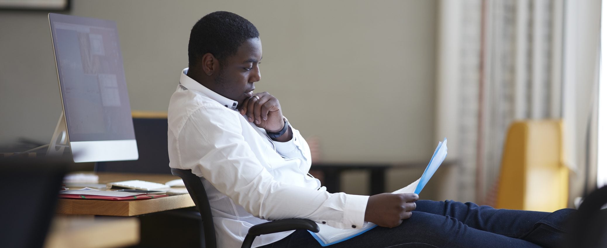 A man, reclining in his desk chair, reads through important financial and insurance documents.