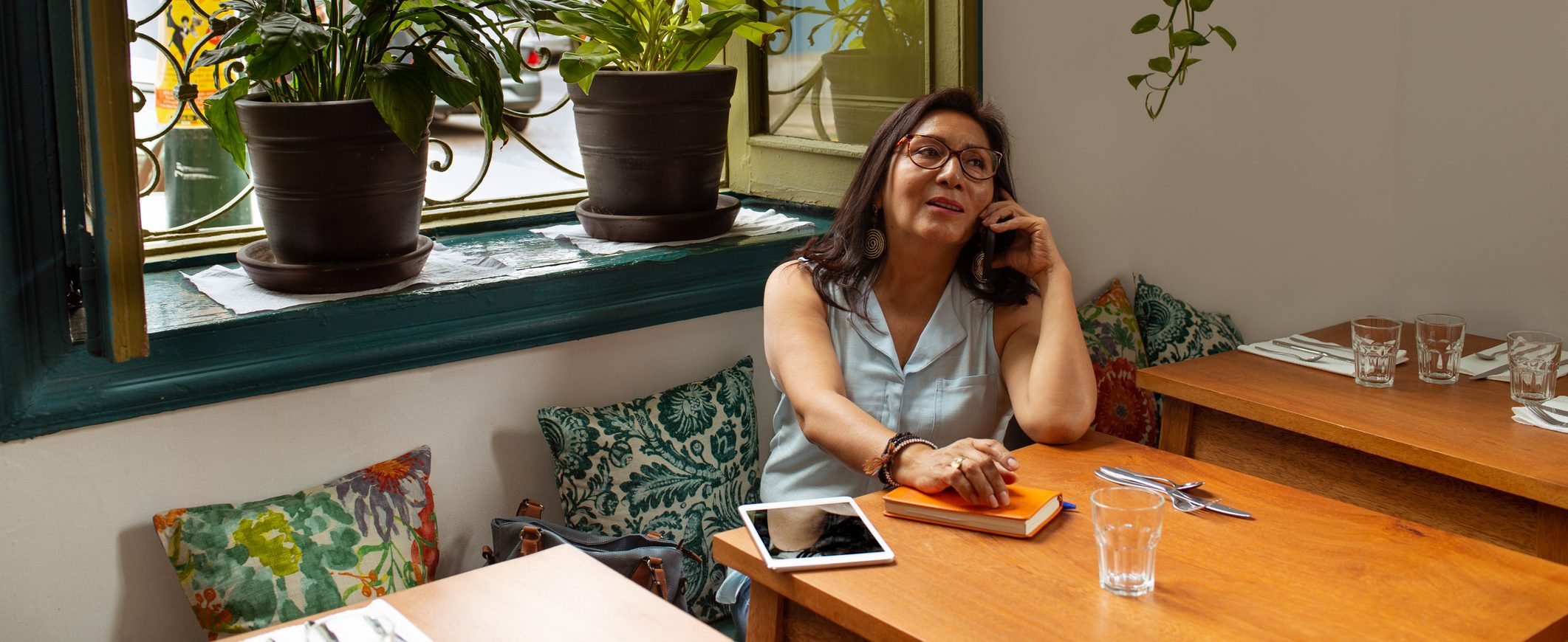 A woman, sitting at a table, talks on the phone with her insurance representative.