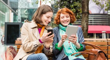 Two women look at their smart devices.