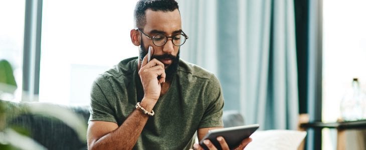 A man, looking pensive, reads something on his tablet computer.