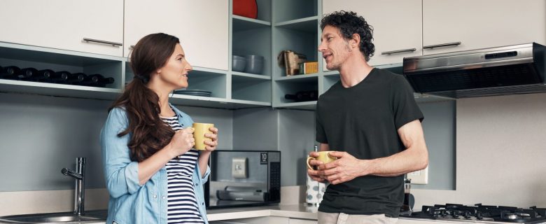 A man and a woman, drinking coffee and having a conversation in their kitchen.