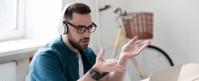 A man wearing headphones and sitting at his desk, in an online video meeting.