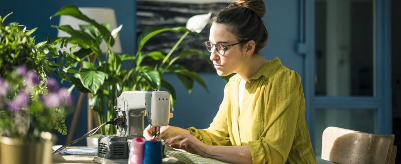 A woman sitting at home and using a sewing machine.