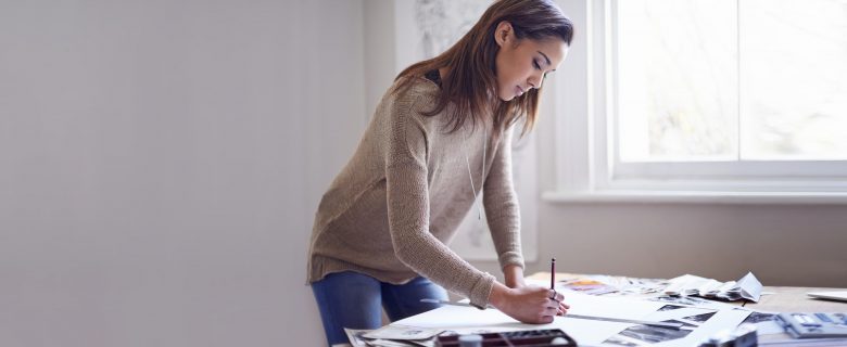 A woman standing next to a work table with a pencil in her hand.