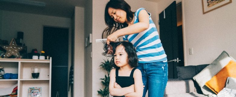 A woman gives her young daughter a haircut in their home living room.