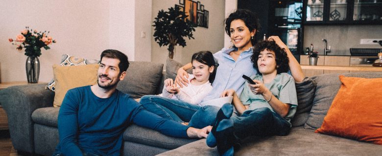 A family of four enjoys watching a movie together on the couch at home.