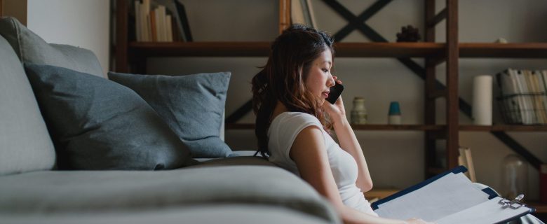 A woman talks on the phone while looking at a notebook.