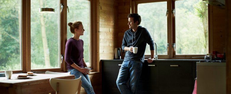 A woman and man talk while holding coffee mugs.