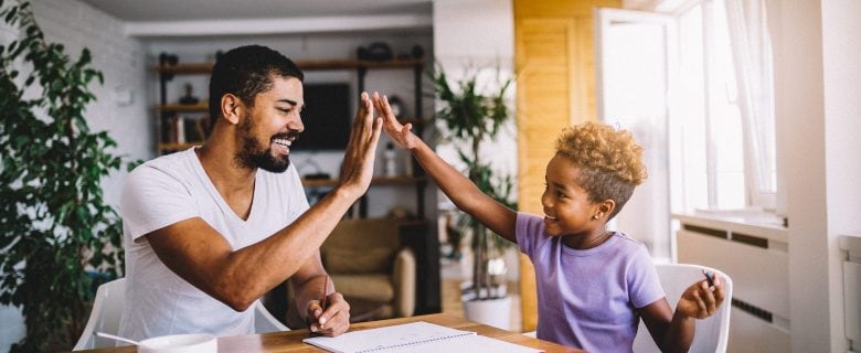 A man high fives his young son after helping him with his homework.