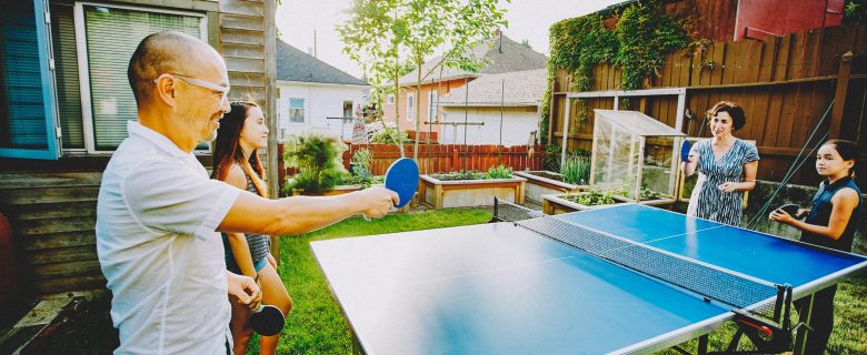 A family of four enjoys a game of ping-pong in their backyard.