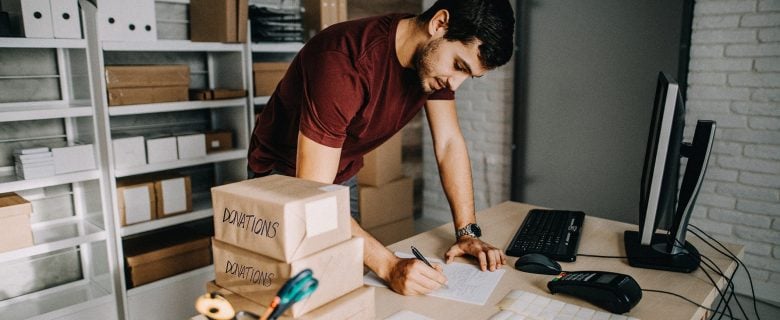 A man writing down some notes next to several packages labeled 'donations.'