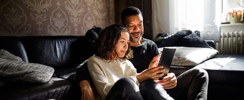 A couple sits in front of a couch reviewing information on a tablet.