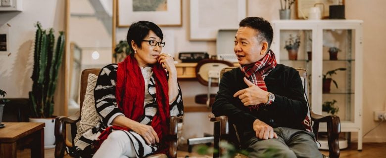 A woman and man sit side by side on chairs talking.