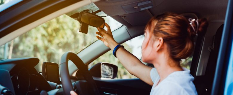 A woman in a car adjusts her rear-view mirror.