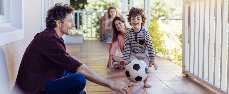 A family of four having fun on the front porch with a soccer ball.