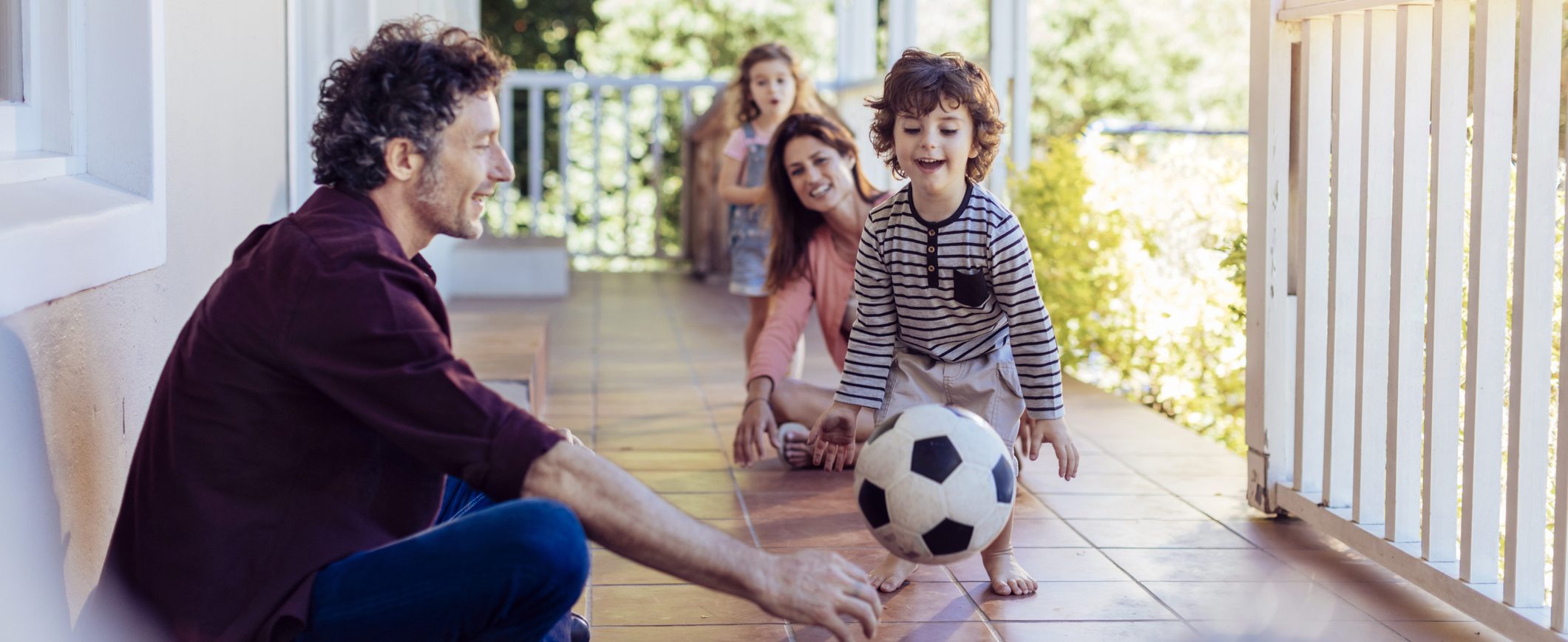 A family of four having fun on the front porch with a soccer ball.