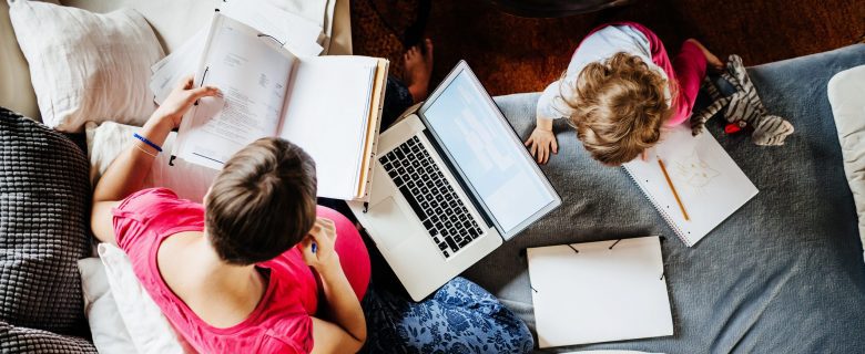 A pregnant woman looking at files with a laptop computer and her young daughter next to her.