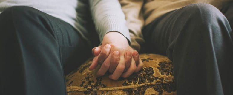 Closeup of two people on a couch holding hands.