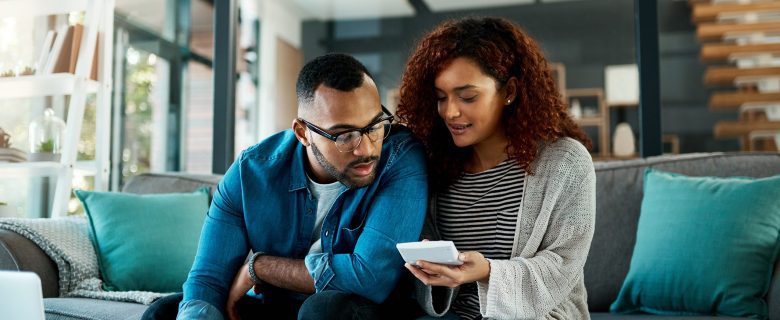 A man and woman sit on a couch looking at a phone together.