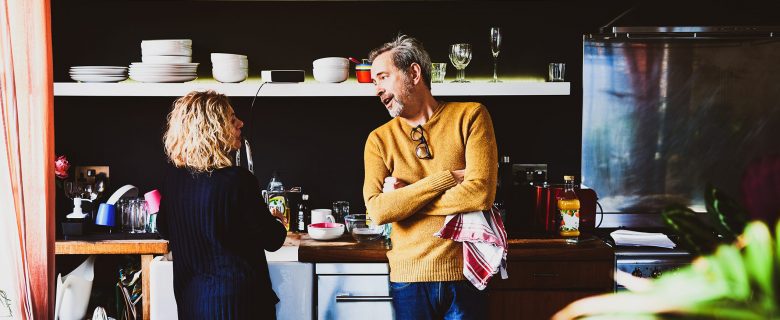 A man and woman talk to each other in a kitchen. 