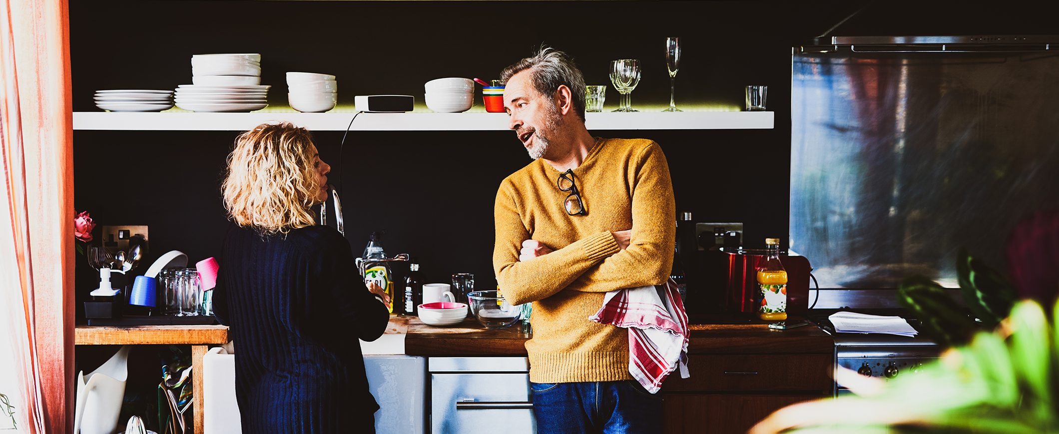 A man and woman talk to each other in a kitchen.