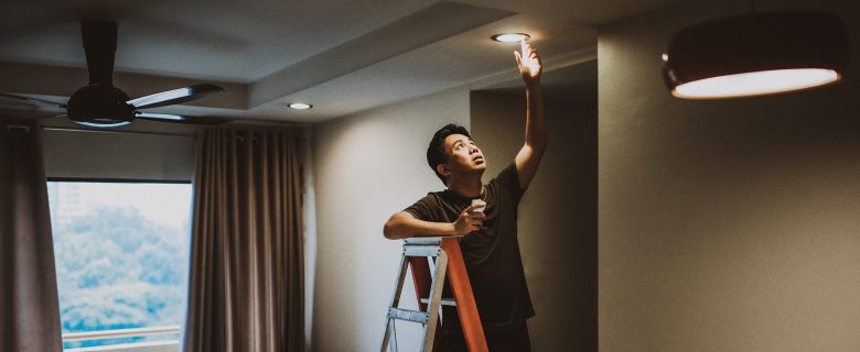 A man on a ladder adjusts a ceiling light bulb. 