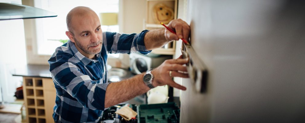 A man uses a level and a pencil to measure for a DIY installation in his home.