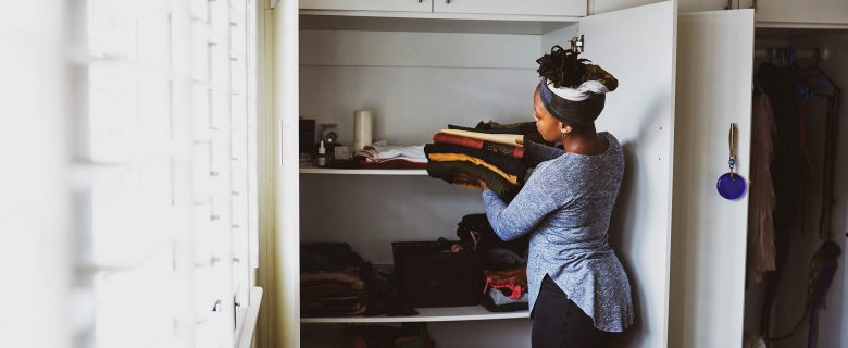A woman puts folded linens into a hall closet.