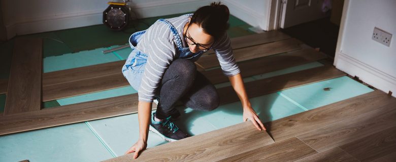 A woman installs a hardwood floor.