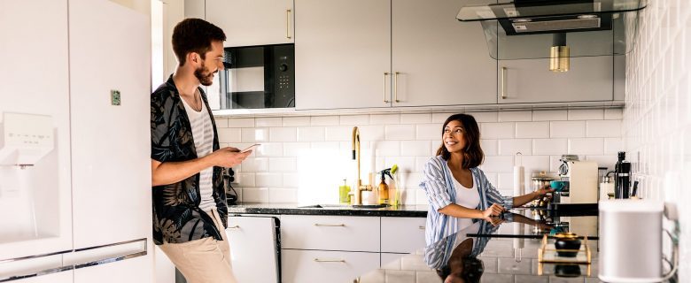 A man and a woman talking in their kitchen, the woman making a pot of coffee.